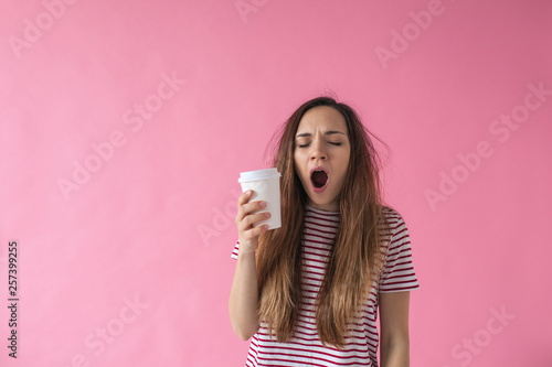 Cute girl with a glass of coffee in hand is yawning. She can't wake up. photo