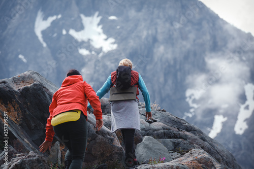 two female tourists go to the high mountain, around the snowy peaks and fog