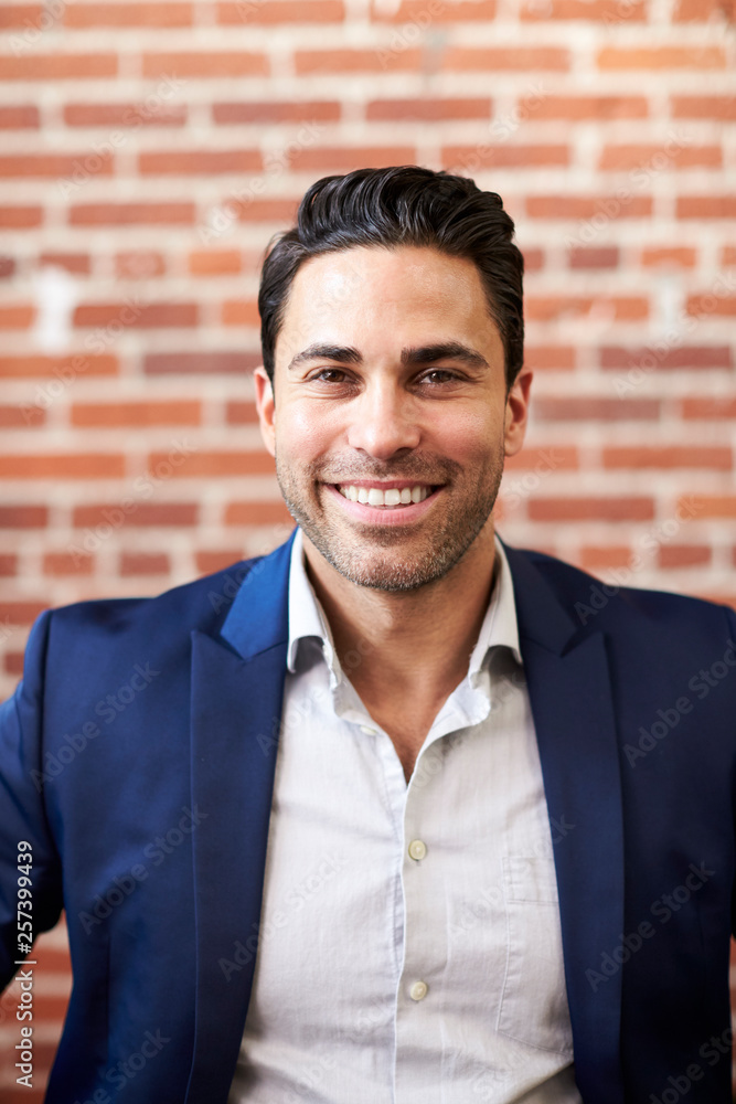 Portrait Of Smiling Mature Businessman Standing Against Brick Wall In Modern Office Portrait Of Smiling Mature Businessman Standing Against Brick Wall In Modern Office