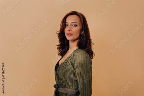 Attractive european woman in green shirt looking at camera. Young woman having fun, beige wall on background.