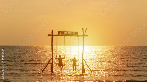 silhouette of happy couple playing swing over the sea with summer sign. happy summer vacation concept