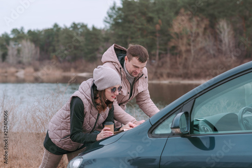 Young romantic couple is watching road map on hood of car near the river. © Ira_Shpiller