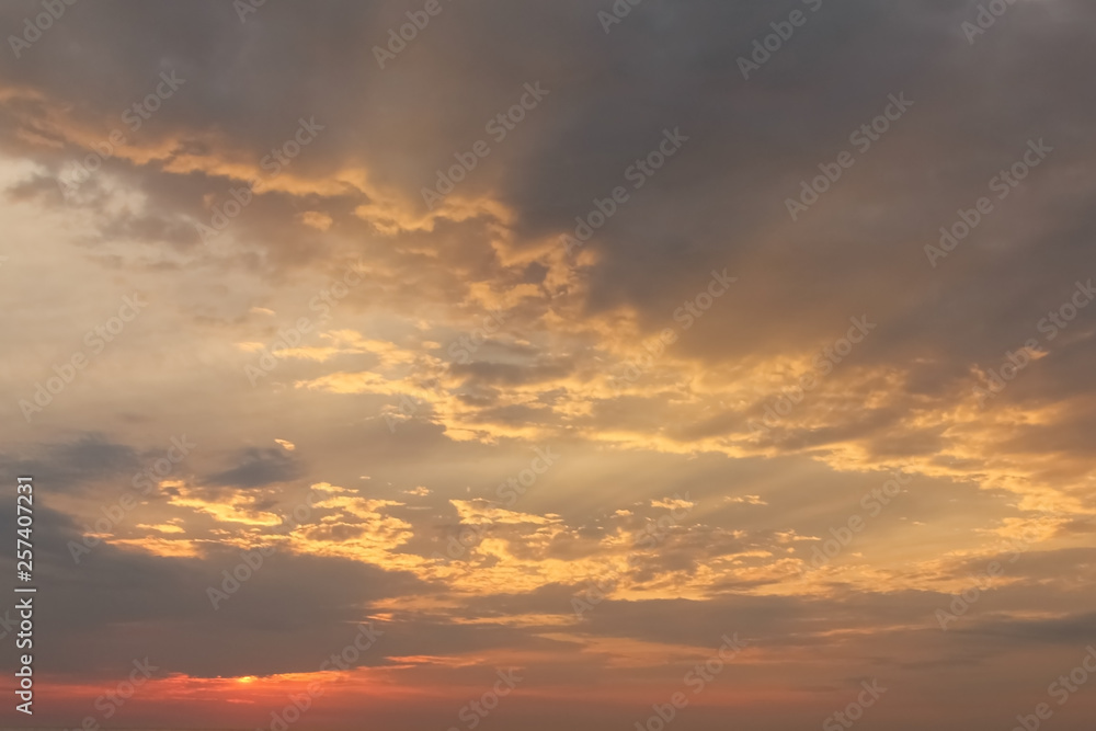 Dramatic sunset sky with orange colored clouds and last rays of the sun, colorful evening background