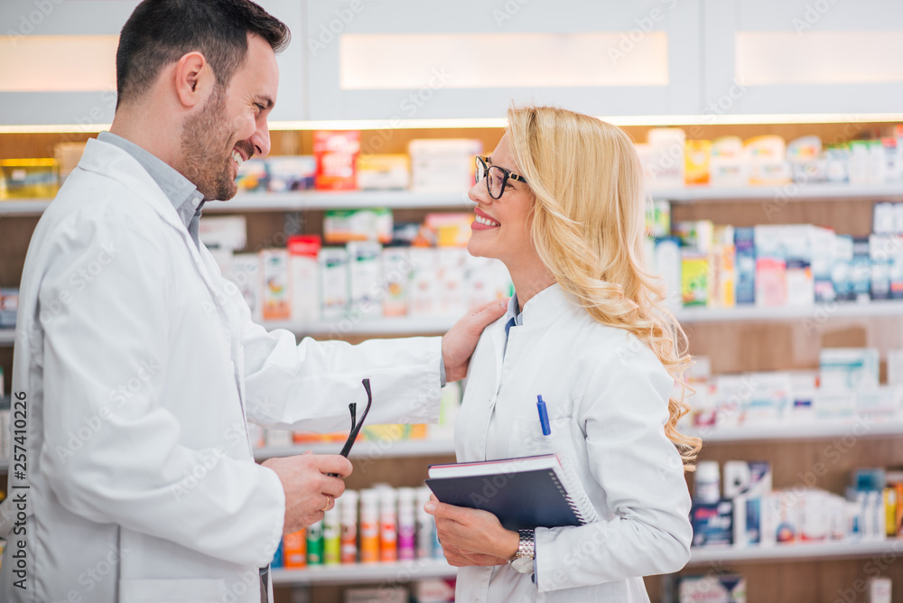 Two smiling healthcare workers looking at each other at modern pharmacy.