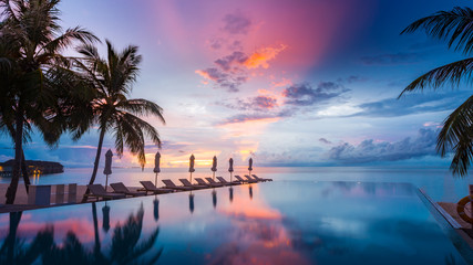 Beautiful poolside and sunset sky. Luxurious tropical beach landscape, deck chairs and loungers and water reflection