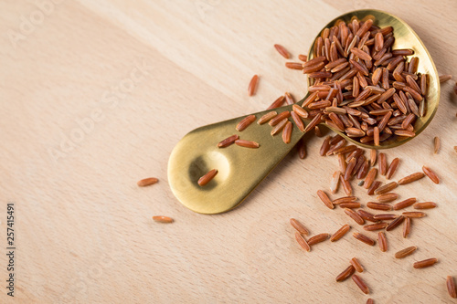 Rotschaliger roher Roter Jasmin Reis auf Gold Metall Löffel und Holz Hintergrund, ist eine Spezialität aus Kambodscha Asien photo