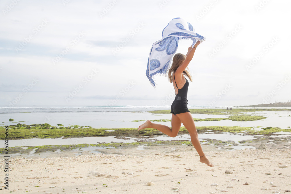  Beautiful teenager girl jumping on the beach and holding the scarf, freedom and travel concept