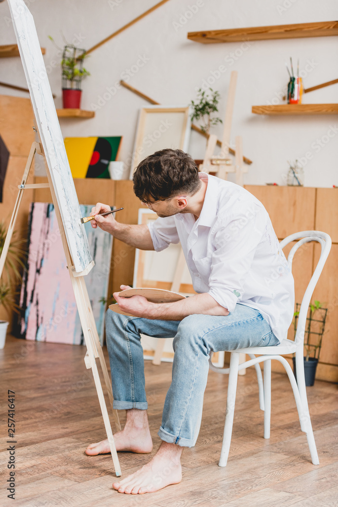 pensive artist in white shirt and blue jeans painting on canvas