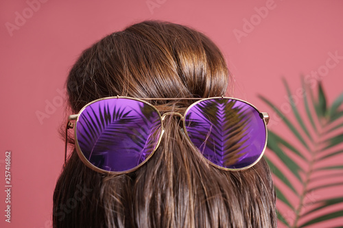 Young woman with hair bun and sunglasses on color background