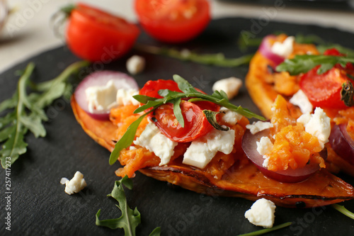 Baked sweet potato with cheese and vegetables on slate plate, closeup