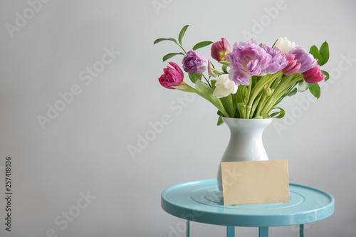 Bouquet of beautiful flowers with card on table against grey background