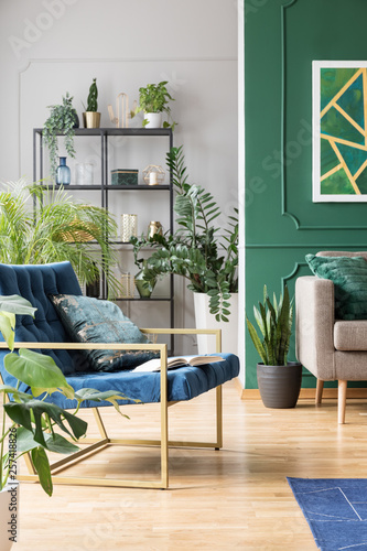 Petrol blue settee with pillow in fashionable living room with green wall, brown couch and urban jungle photo