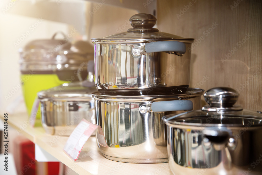 Stainless steel kitchenware set on shelves, shallow depth of field image. Warm light. Backlight on the left. Stainless steel kitchenware set on shelves, shallow depth of field image. Warm light. Backlight on the left.