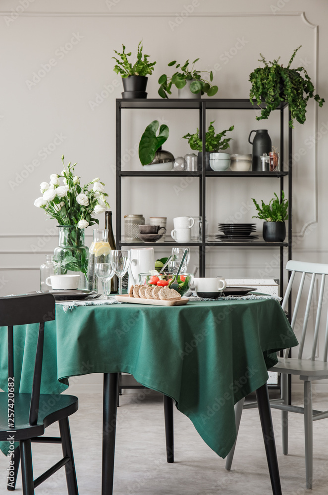 Obraz premium Round kitchen table with breakfast and roses in glass vase in grey interior with industrial metal shelf with dishes