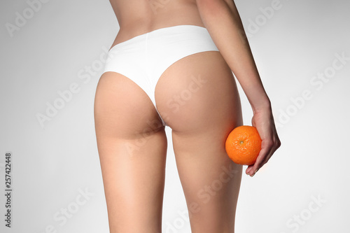 Beautiful young woman with orange on light background. Problem of cellulite