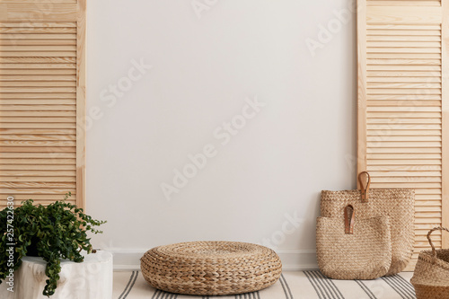 Empty white wall between wooden screen in bright interior with wicker pouf and straw bags photo