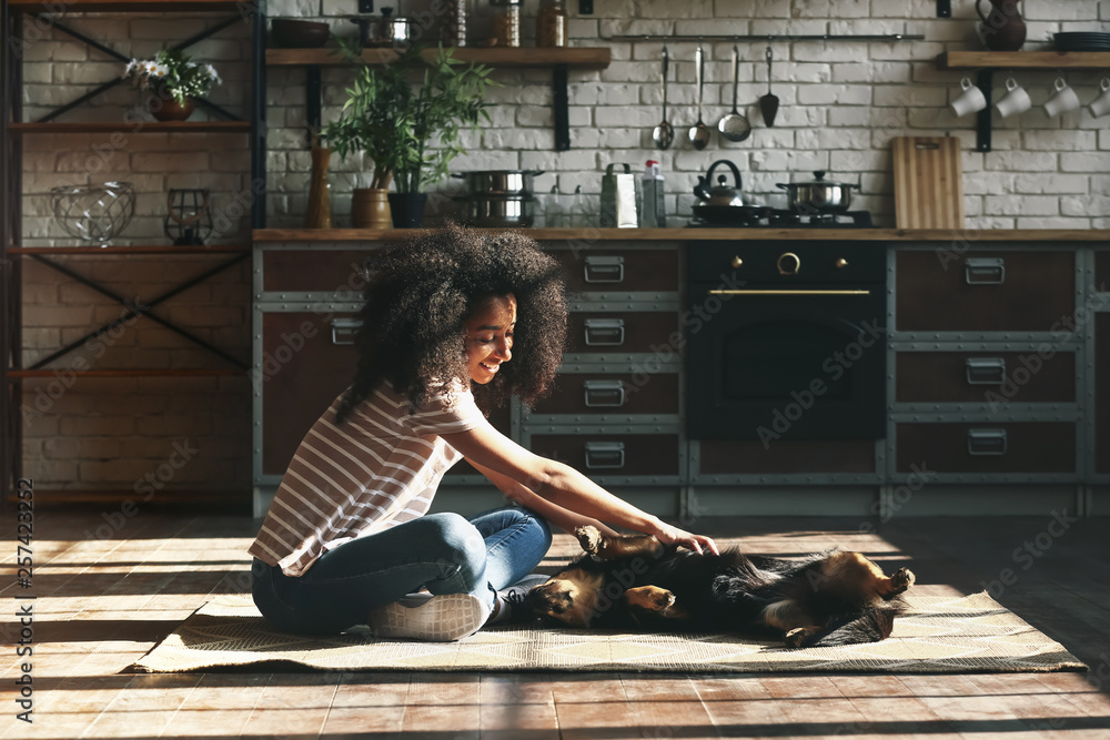 African-American woman with cute funny dog at home - obrazy, fototapety, plakaty 