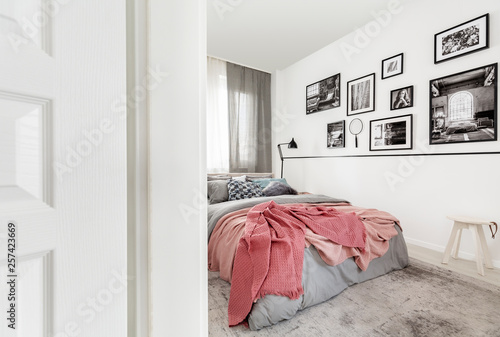 Gallery of posters on white wall in modern bedroom interior with pink sheets on bed. Real photo © Photographee.eu