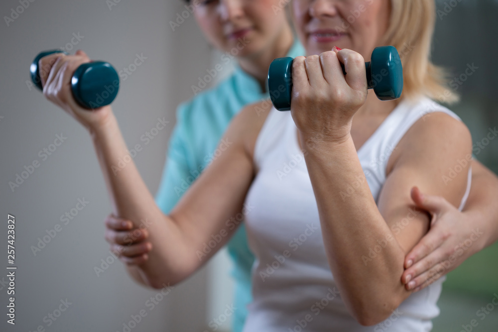 Professional physiotherapist helping senior woman to lift hand weights Professional physiotherapist helping senior woman to lift hand weights
