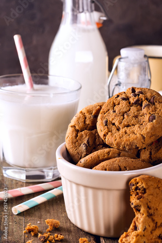 Bowl with tasty american chocolate chip cookies and glass of milk on wooden table