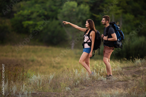 A man and a woman are hiking in the mountains with backpacks. The girl points the right way
