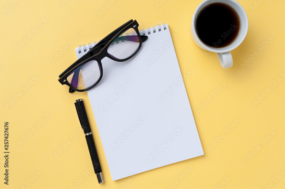 Coffee, notebook, eyeglasses and office stationery on bright yellow background Coffee, notebook, eyeglasses and office stationery on bright yellow background