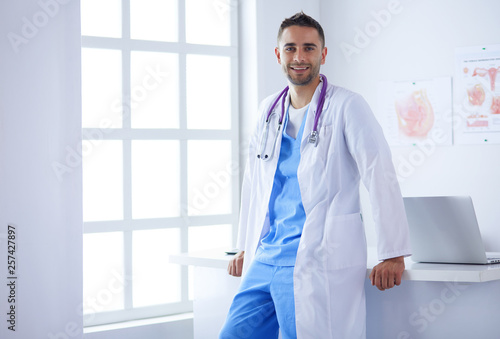 Young and confident male doctor portrait standing in medical office. photo