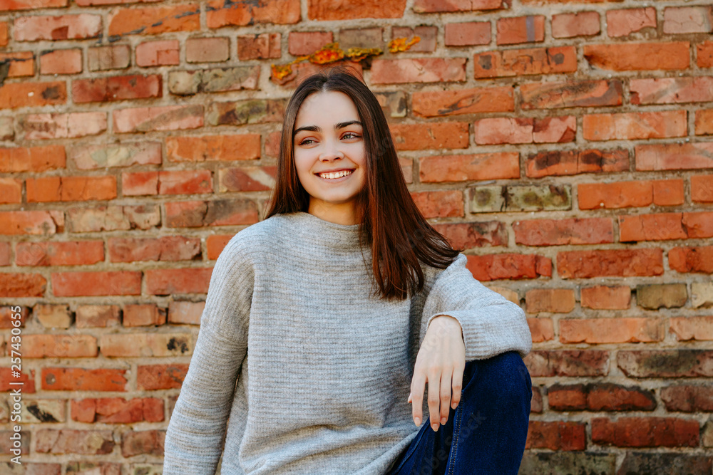 Young beautiful girl sitting on a brick wall background. Spring mood Young beautiful girl sitting on a brick wall background. Spring mood
