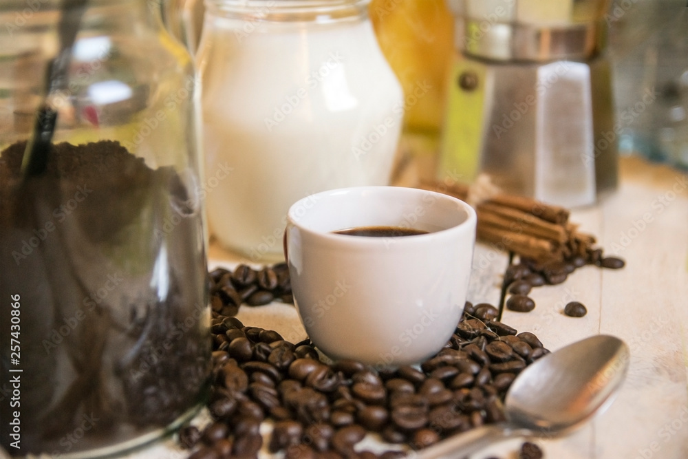 Cup of coffee, milk, cinnamon and some coffee beans on a wooden table in a rustic kitchen. Empty copy space for Editor's text. Cup of coffee, milk, cinnamon and some coffee beans on a wooden table in a rustic kitchen. Empty copy space for Editor's text.