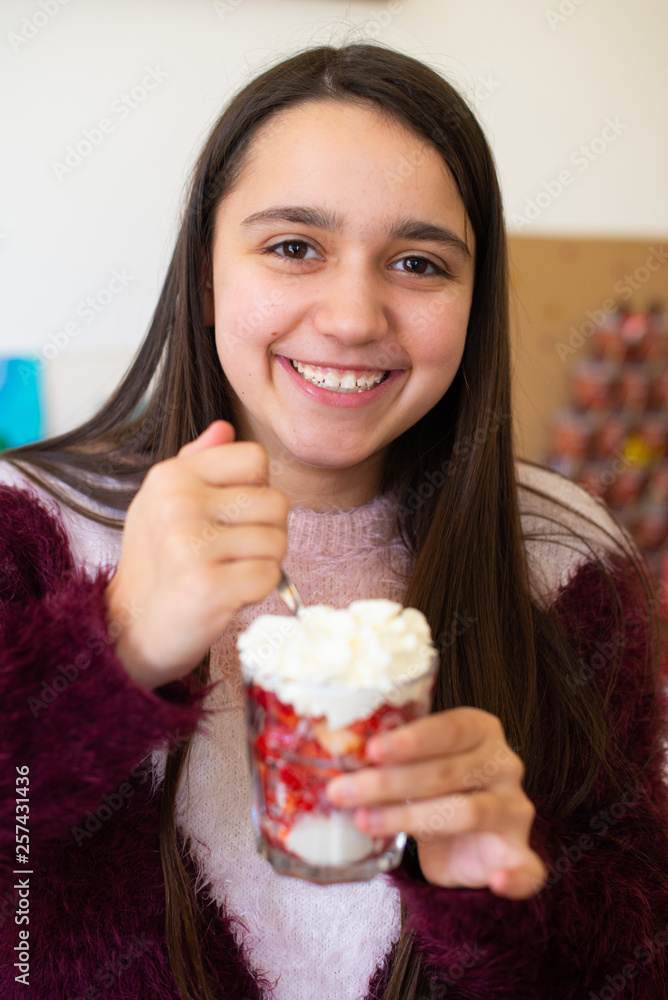 teen ager girl eating an ice cream with strawberries and cream - happy girl eating dessert - girl portraits teen ager girl eating an ice cream with strawberries and cream - happy girl eating dessert - girl portraits