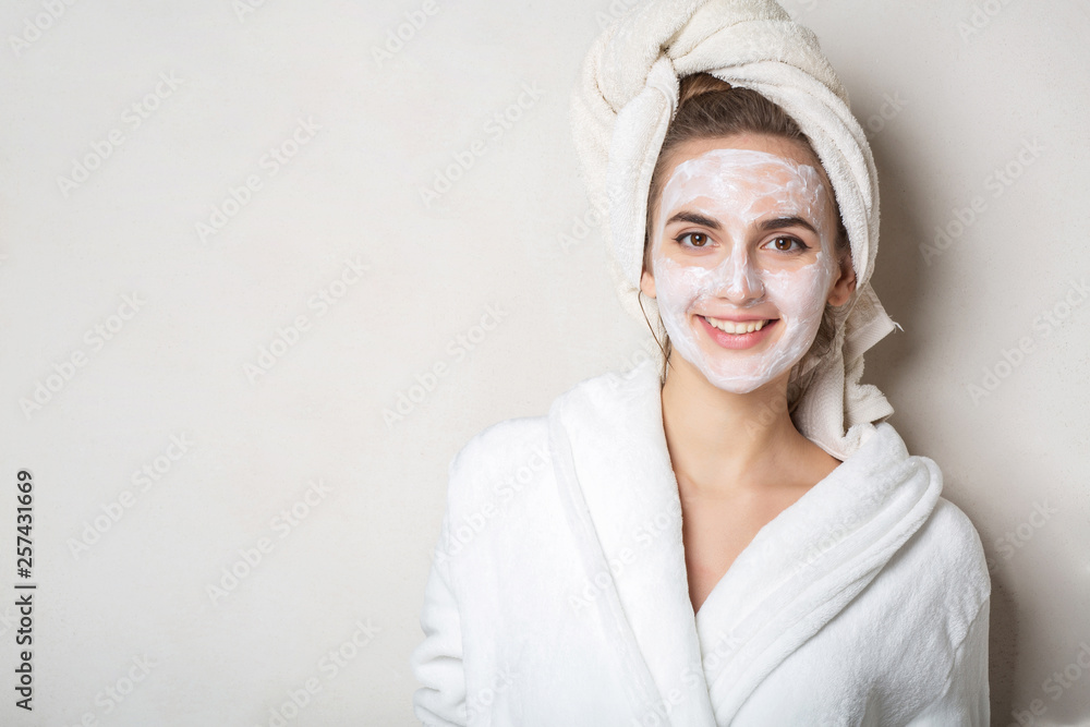Obraz premium Cheerful brunette model with moisturizing cream mask and bath towel on head. Empty space