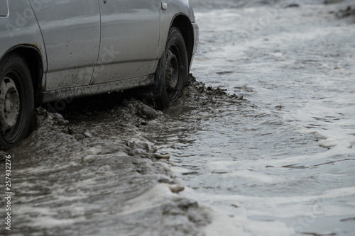 Poor road condotions - car wheel in melting show puddle.