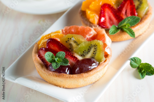 Fresh fruit and berry tart dessert with toss sugar on wooden background. Delicious sweet cake with raspberries  grapes  strawberries  cherry  kiwi  grapefruit and cream.