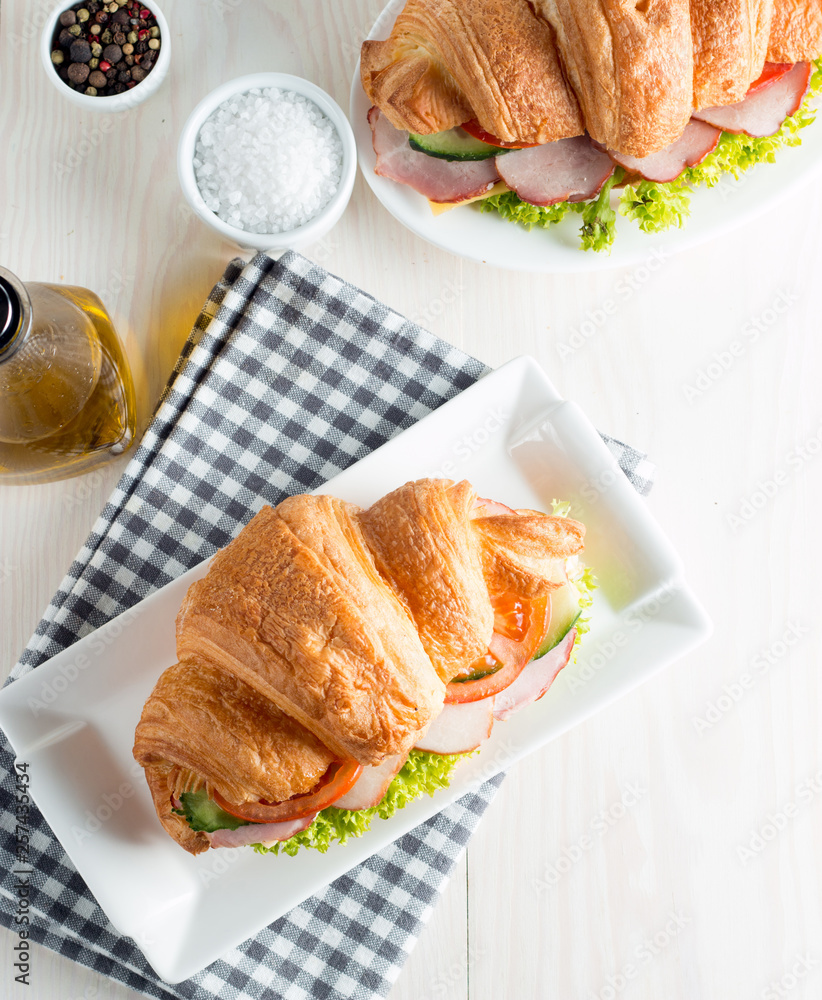 Fresh croissant or sandwich with salad, ham, jamon, prosciutto, salami, cheese, chicken, tomatoes on wooden background. Morning breakfast concept. Healthy and fast food. Fresh croissant or sandwich with salad, ham, jamon, prosciutto, salami, cheese, chicken, tomatoes on wooden background. Morning breakfast concept. Healthy and fast food.