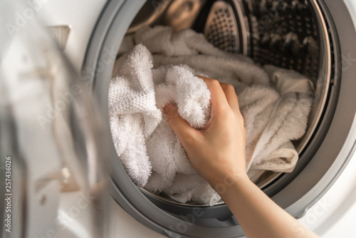 Close up of woman hand loading white towels into the washing machine