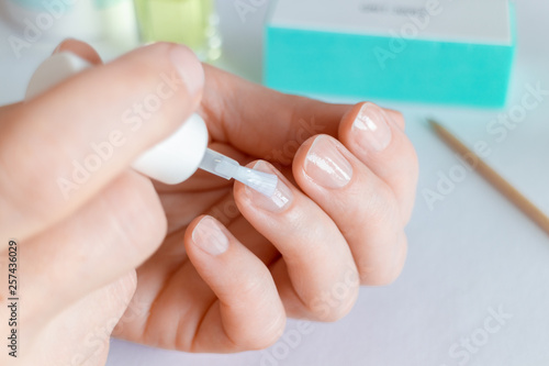 Woman doing at-home manicure, applying nail conditioner or base coat. photo