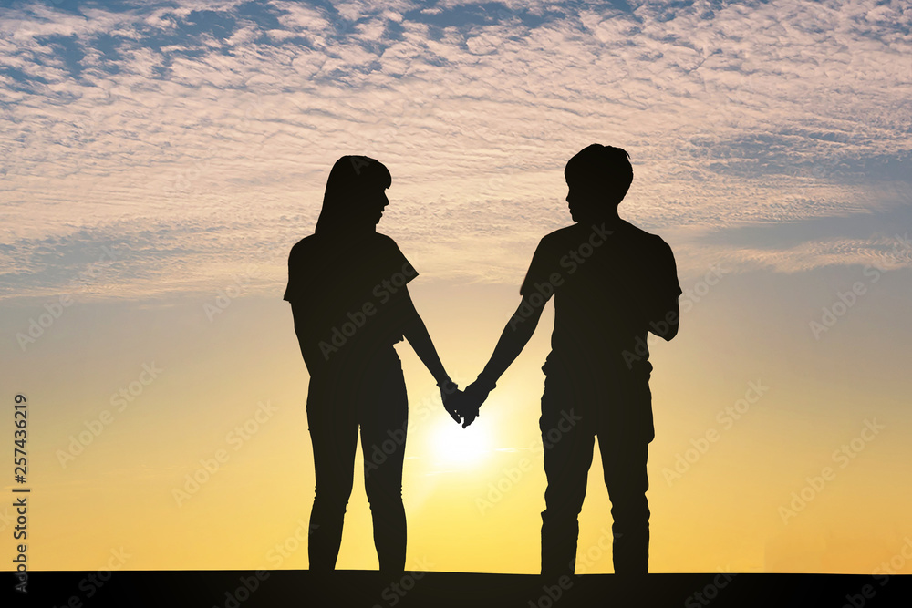 Silhouette men and women hold hands on the background of the sunset.