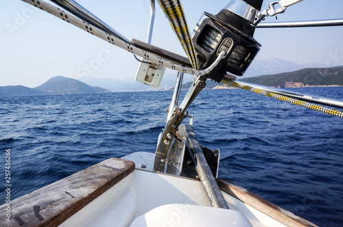 Image of the bow of a cruising sailing ship with roller furling gear and an anchor against dark blue water on a bright sunny day photo