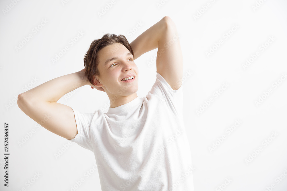 Looking for the best moment. Young dreaming smiling teenager waiting for chanses isolated on a gray background. Dreamer is staying with the romantic sight at studio in white T-shirt with crossed hands Looking for the best moment. Young dreaming smiling teenager waiting for chanses isolated on a gray background. Dreamer is staying with the romantic sight at studio in white T-shirt with crossed hands