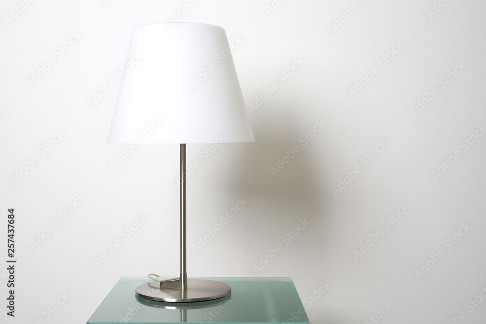 Stylish design lamp on glass table in front a white plastered wall with copy space. Stylish design lamp on glass table in front a white plastered wall with copy space.