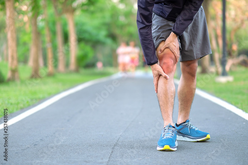 Young fitness man holding his sports leg injury. muscle painful during training. Asian runner having knee ache and problem after running and exercise outside morning. sport and healthy concepts