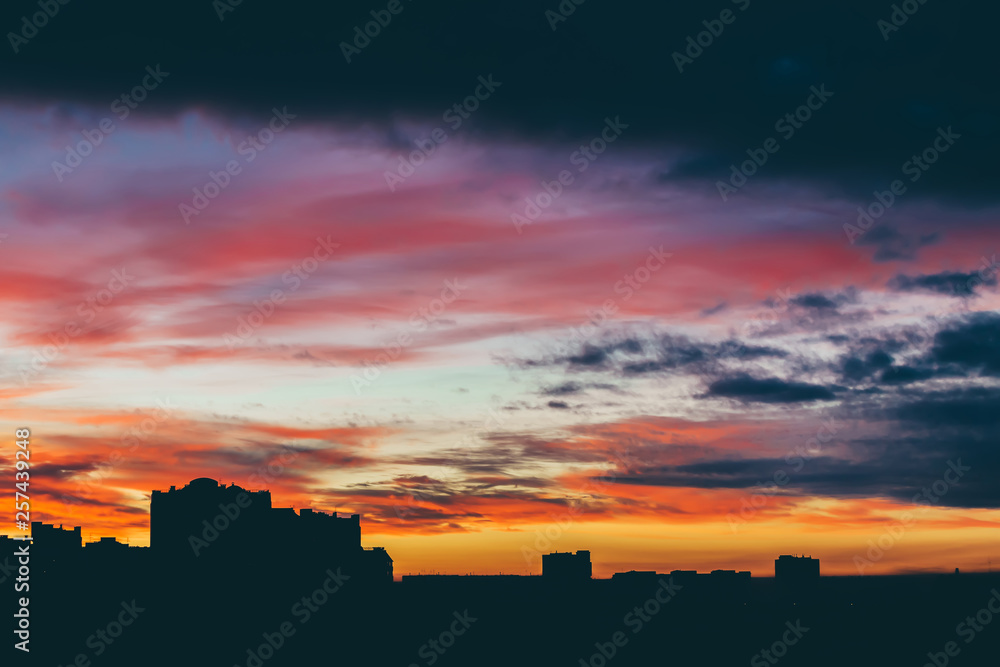 Cityscape with wonderful varicolored vivid dawn. Amazing dramatic multicolored cloudy sky above dark silhouettes of city buildings. Atmospheric background of sunrise in overcast weather. Copy space. Cityscape with wonderful varicolored vivid dawn. Amazing dramatic multicolored cloudy sky above dark silhouettes of city buildings. Atmospheric background of sunrise in overcast weather. Copy space.