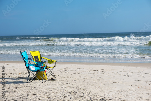 Two colorful beach chairs set up on the beach with waves rolling in and no people prese
