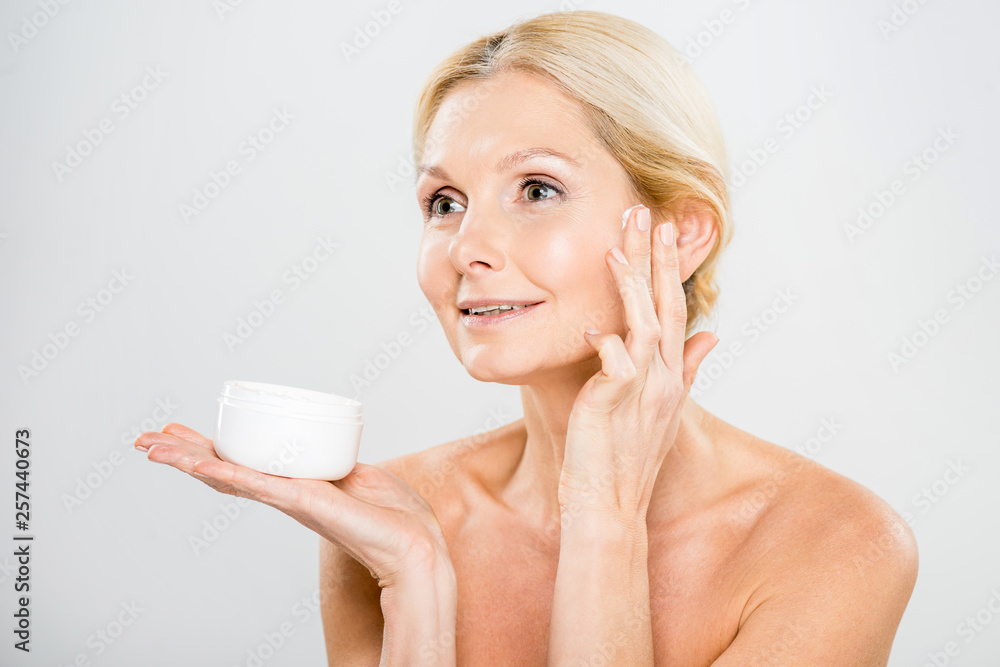 beautiful and smiling woman looking away and applying cosmetic cream beautiful and smiling woman looking away and applying cosmetic cream