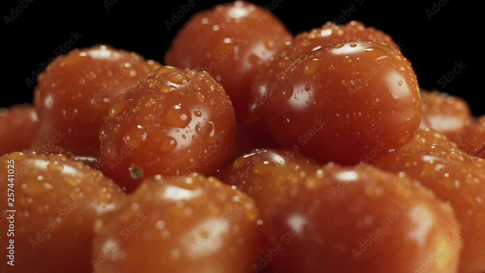 Rotating ripe cherry tomatoes in drops of water on a black background close-up. Rotating ripe cherry tomatoes in drops of water on a black background close-up.