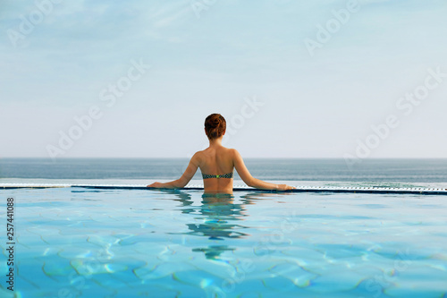 Luxury vacation travel woman relaxing in infinity swimming pool on summer beach resort. Spa relaxation watching in nature landscape background.