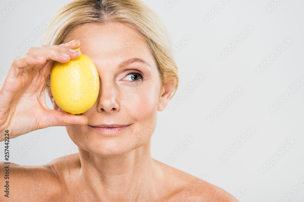 beautiful and mature woman holding ripe lemon and looking away isolated on grey beautiful and mature woman holding ripe lemon and looking away isolated on grey