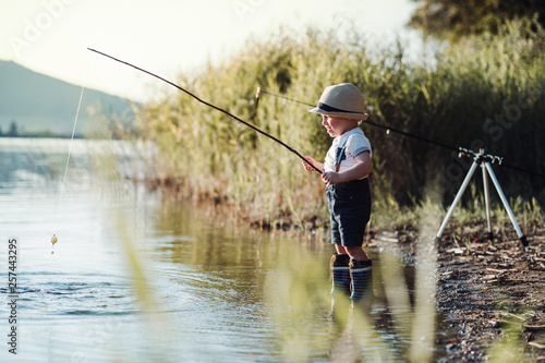 A small toddler boy standing by a lake at sunset, fishing. Copy space.