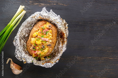 Baked potatoes in foil with bacon, onions and mushrooms on a gray wooden table. Copy space. Top view