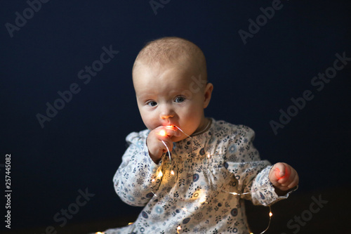 Obraz na plátně Baby in dress on dark blue background with garland